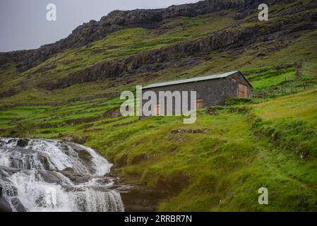 Des cascades d'eau passent devant une étable à moutons sur une pente raide sur l'île de Vagar dans les îles Féroé. Banque D'Images