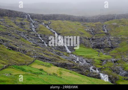 Cascades d'eau sur une pente au-dessus du village de Tjørnuvik, dans les îles Féroé. Banque D'Images