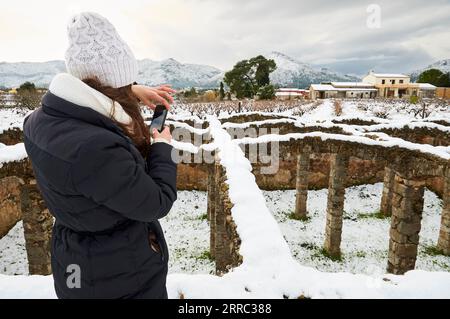 Randonneuse photographiant Bassa dels Arcs, un réservoir d'eau du XVIIIe siècle, couvert de neige fraîche (Xaló, Vall de Pop, Marina Alta, Alicante, Espagne) Banque D'Images