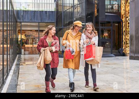 Heureux diverses femmes matures riant tout en faisant du shopping près de la décoration des lumières de noël Banque D'Images