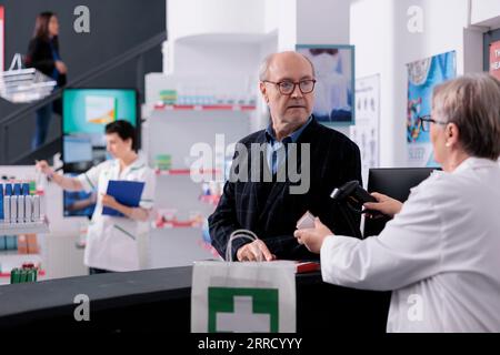 Un employé de la pharmacie scannant l'emballage solaire pour indiquer le prix à l'acheteur à la caisse enregistreuse du magasin médical. Vieil homme choisissant le produit dermatologique de protection solaire dans la pharmacie, acheter de la crème solaire à la caisse Banque D'Images