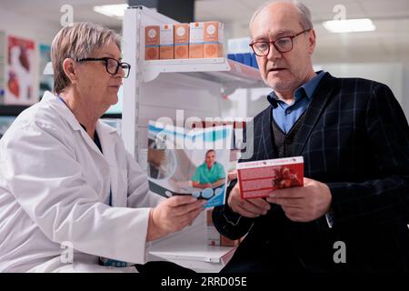 Travailleur de pharmacie faisant la consultation pharmaceutique d'homme âgé dans la pharmacie, conseillant les médicaments de coeur. Patient âgé qui choisit des suppléments pour le traitement des maladies cardiovasculaires Banque D'Images