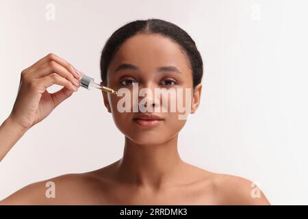 Belle femme appliquant du sérum sur son visage sur fond blanc Banque D'Images