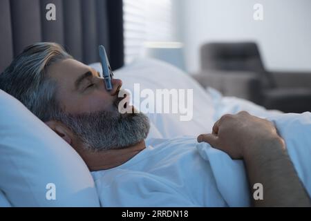 Homme dormant avec des épingles à linge sur son nez dans le lit à la maison. Problème de ronflement Banque D'Images