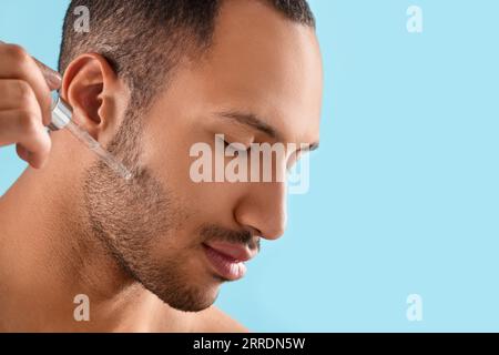 Bel homme appliquant le sérum cosmétique sur le visage sur fond bleu clair, closeup. Espace pour le texte Banque D'Images
