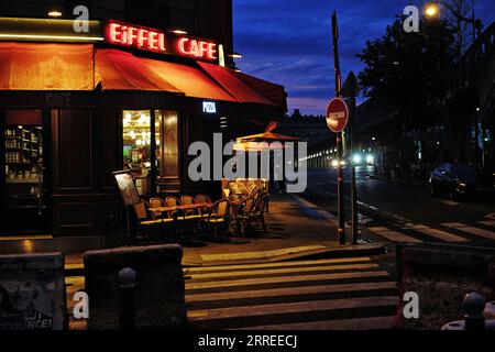 Café Eiffel en fin de soirée d'été, enseigne au néon rouge brillant sur le ciel bleu nocturne, chaises de café, lampadaires sur Grenelle et Pont de Bir-Hakeim Banque D'Images