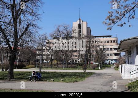 220322 -- BELGRADE, le 22 mars 2022 -- des gens s'assoient sur un banc près du bâtiment de commandement bombardé de l'armée de l'air yougoslave à Belgrade, Serbie, le 21 mars 2022. À Belgrade, les bombardements de l'OTAN laissent de nombreuses cicatrices. Les bombardements de l'OTAN en Yougoslavie ont commencé le 24 mars 1999. Au cours de cette attaque militaire de 78 jours, 2 500 civils ont été tués et environ 25 000 objets ont été endommagés, dont des aéroports, des hôpitaux, des écoles, des monuments culturels et des infrastructures routières, selon le gouvernement serbe. SERBIE-BELGRADE-HISTOIRE ZhengxHuansong PUBLICATIONxNOTxINxCHN Banque D'Images