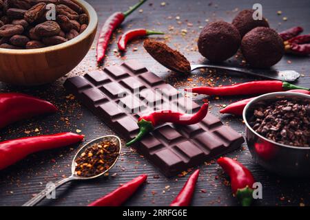 Barre de chocolat noir, piment rouge piment piment de Cayenne, épices piment chaud sec, fèves de cacao en poudre, conception savoureuse de nourriture sur fond en bois noir Banque D'Images