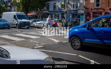 Grantham Lincolnshire - passage à niveau Zebra ou un passage pour piétons sur une rue très fréquentée avec une personne en fauteuil roulant poussé à travers la route Banque D'Images