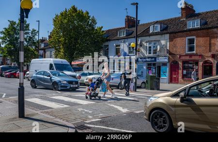 Grantham Lincolnshire - passage Zebra ou un passage pour piétons dans une rue très fréquentée avec une jeune mère traversant avec son enfant dans une poussette Banque D'Images