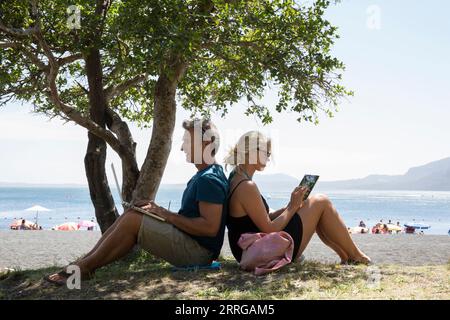 Couple mature assis à l'ombre sur le lac en utilisant l'ordinateur et la tablette Banque D'Images