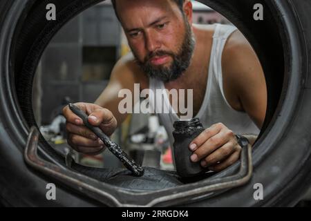 l'homme applique de la colle avec un pinceau sur un pneu pour le réparer dans son garage Banque D'Images