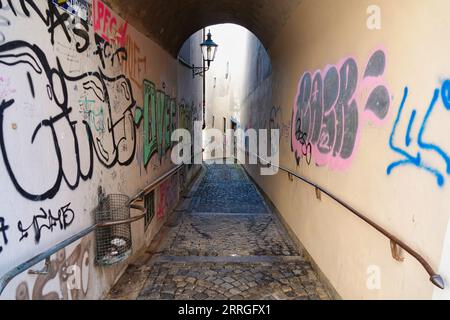 Une vieille allée voûtée avec des graffitis, une poubelle et une lanterne sur le mur à Augsbourg, en Allemagne. Banque D'Images