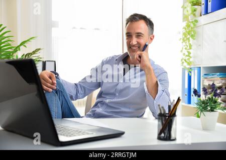 Homme adulte entrepreneur assis confortablement dans une chaise fièrement à son bureau dans un bureau regardant un écran d'ordinateur portable Banque D'Images