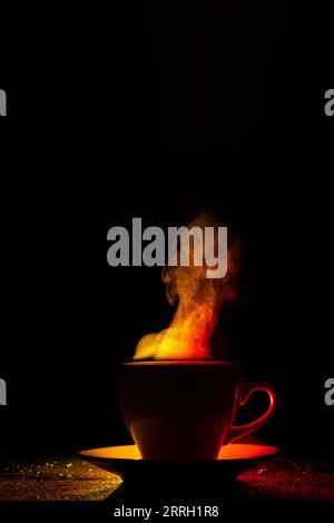 Un mug avec une boisson chaude et de la vapeur bouclés se lève, illuminé en rouge-jaune, orange sur fond noir, espace de copie, créatif, silhouette. Matin Banque D'Images