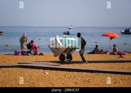 220625 -- GOZO, le 25 juin 2022 -- un membre du personnel transporte des chaises de plage dans un chariot sur la plage de Ramla, sur l'île de Gozo, Malte, le 25 juin 2022. Photo de /Xinhua MALTE-VAGUE DE CHALEUR JonathanxBorg PUBLICATIONxNOTxINxCHN Banque D'Images