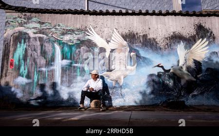 220626 -- LIJIANG, le 26 juin 2022 -- Liu Zhicheng fait une pause avec sa peinture murale en arrière-plan dans le comté de Yongsheng, ville de Lijiang, province du Yunnan dans le sud-ouest de la Chine, le 24 juin 2022. Un peintre mural à but non lucratif après les années 95, originaire du comté de Yongsheng dans la ville de Lijiang, a gagné en popularité auprès des villageois de sa ville natale et des internautes sur les plateformes de médias sociaux. L'artiste mural nommé Liu Zhicheng a peint plus de 20 peintures murales de thèmes différents dans de nombreux villages de sa ville natale. Ses œuvres d'art ont ajouté de la couleur aux villages et ont attiré de nombreux touristes comme les courtes vidéos d'enregistrement Banque D'Images