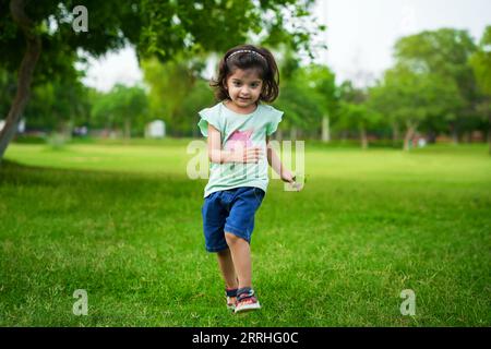 Gaie et insouciante petite fille indienne courant au parc d'été ou au jardin. Banque D'Images