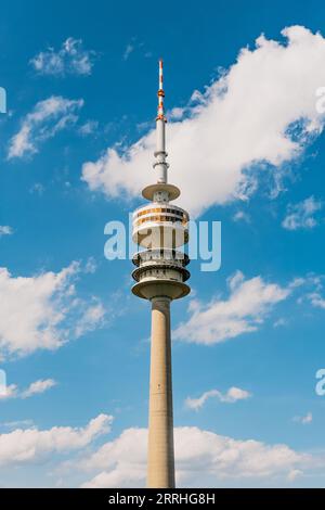 Tour Olympiaturm haute et pointue au centre avec un ciel d'été bleu dramatique et des nuages blancs en arrière-plan Banque D'Images