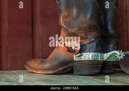 Vieilles bottes de cow-boy en cuir marron avec éperons sur une surface en bois à la lumière du soleil Banque D'Images