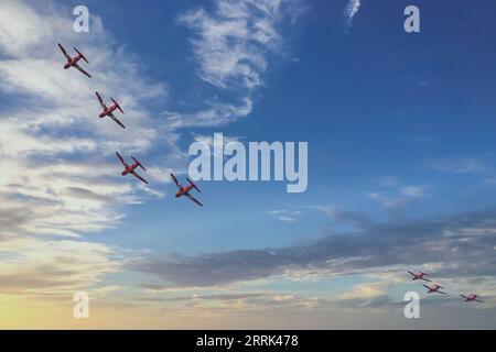 Sept jets Red Arrow Hawk éclatants s'envolent dans l'éblouissant coucher de soleil en soirée, créant un spectacle aérien spectaculaire. Banque D'Images