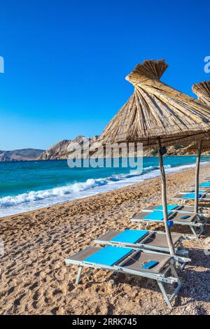 Croatie, baie de Kvarner, comté de Primorje Gorski Kotar, île de Krk, chaises longues et parasols de chaume sur la plage de galets à Baska Banque D'Images