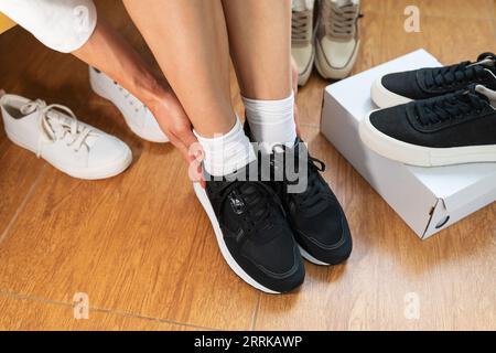 Une fille dans un magasin choisit des chaussures tout en étant assise dans la cabine d'essayage du magasin. Met des chaussures et sélectionne le style et la taille appropriés du vari Banque D'Images