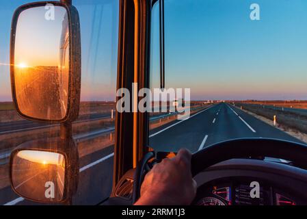 Vue depuis le siège du conducteur d'un camion, avec une route droite devant et le soleil se levant. Banque D'Images