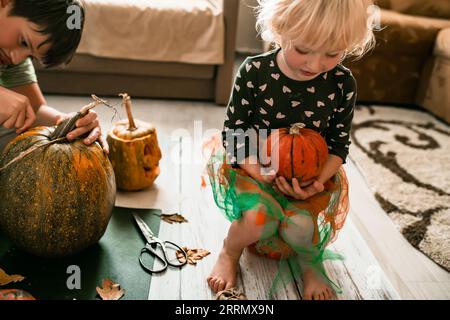 Petites sorcières en devenir ! Les enfants en costume sculptent des citrouilles pour une nuit effrayante d'Halloween. Banque D'Images