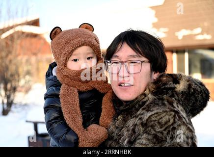 230113 -- GENHE, 13 janvier 2023 -- cette photo prise le 13 janvier 2023 montre Juele avec son enfant dans une nouvelle communauté de relocalisation dans le canton d'Aoluguya Ewenki dans la ville de Genhe, dans la région autonome de Mongolie intérieure du nord de la Chine. Tous les deux ou trois jours, Juele Bulituotian se dirigera vers la chaîne forestière de Jinhe, à environ 80 kilomètres de Genhe City. C'est là que le berger d'Aoluguya Ewenki, âgé de 39 ans, portant un manteau de fourrure traditionnel, trouvera son renne de recherche de nourriture. Au lieu de garder des rennes dans une grange, les éleveurs Ewenki laissent les animaux vivre dans la forêt et les surveillent tous les deux jours. Juele possède plus de 60 rei Banque D'Images