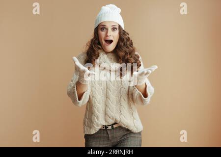 Bonjour hiver. surprise femme élégante en chandail beige, mitaines et chapeau sur fond beige. Banque D'Images