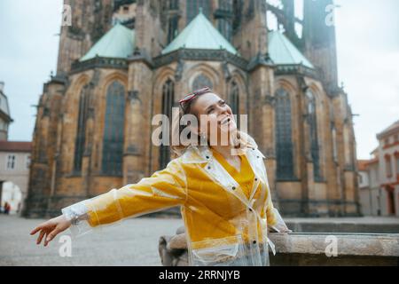 Femme touristique solo souriante élégante en chemisier jaune et imperméable à Prague République tchèque profitant de la promenade. Banque D'Images