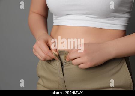 Femme en surpoids essayant de boutonner un pantalon serré sur fond gris, gros plan. Espace pour le texte Banque D'Images