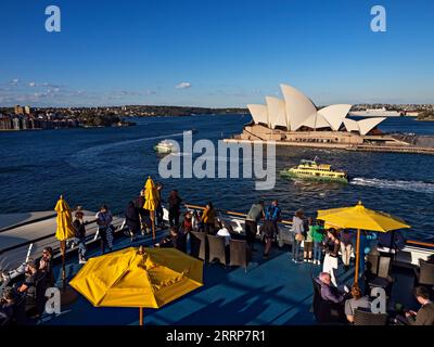 Sydney Australie / Sydney les ferries passent devant l'Opéra de Sydney. Les passagers sur un pont supérieur admirent la vue alors que le navire se prépare à partir. Banque D'Images