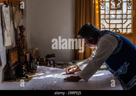 230317 -- JIANCHUAN, le 17 mars 2023 -- Duan Sixing dessine des motifs de sculpture sur bois dans son atelier du comté de Jianchuan, préfecture autonome de Dali Bai dans la province du Yunnan du sud-ouest de la Chine, le 2 décembre 2022. Le comté de Jianchuan, situé dans la préfecture autonome de Dali Bai dans la province du Yunnan, au sud-ouest de la Chine, a une longue histoire dans la sculpture sur bois datant des dynasties Tang 618-907 et Song 960-1279. Les compétences en sculpture se sont progressivement développées, passant d'un relief à une couche à un relief creux à sept couches, et sont maintenant appliquées à la fabrication de pièces d'architecture, de meubles en bois, de peintures murales et de souvenirs touristiques. Un maximum Banque D'Images