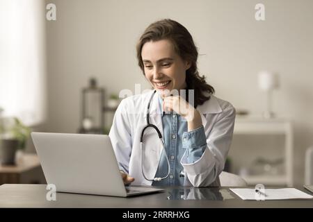 Heureuse jeune femme médecin praticien travaillant à l'ordinateur portable Banque D'Images