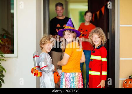 Les enfants trichent ou gâtent le soir d'Halloween. Les enfants habillés à la porte de la maison décorée. Garçon et fille en costume de sorcière et de vampire et chapeau Banque D'Images