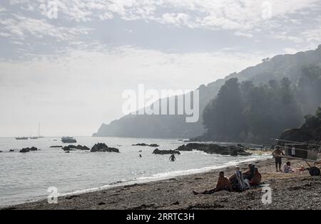 Vue de Cawsand Beach, Cornwall avec des figures de premier plan et une brume de chaleur sur le promontoire lointain à Pier Cellars Banque D'Images