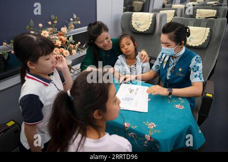 230718 -- MENGLA, 18 juillet 2023 -- Yi Bofeng R interagit avec les passagers à bord du train D887 le 16 juillet 2023. Yi Bofeng est originaire du comté de Mengla dans la province du Yunnan. Après avoir obtenu son diplôme de major laotien dans un collège technique de la capitale provinciale Kunming en 2020, elle a été recrutée comme hôtesse de train dans China Railway Kunming Bureau Group Co., Ltd Le chemin de fer Chine-Laos, un projet historique de coopération de haute qualité ceinture et route, a commencé ses opérations en décembre 2021. Yi était à bord du premier train du chemin de fer, témoin du moment historique de l'exploitation ferroviaire. Le railwa de 1 035 km Banque D'Images