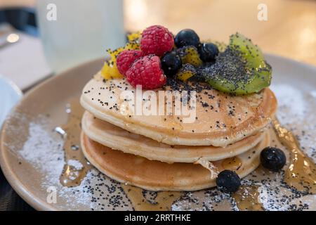Pile de crêpes épaisses et moelleuses à l'américaine servies avec du sirop d'érable versé sur des baies fraîches et du kiwi, saupoudré de graines de pavot Banque D'Images