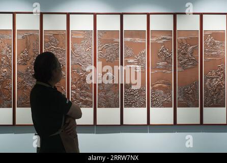 230815 -- NANCHANG, 15 août 2023 -- Huang Junjun regarde ses œuvres de gravure sur cuivre dans un hall d'exposition de sa société dans la ville de Guixi, province de Jiangxi dans l'est de la Chine, le 13 juillet 2023. Gravure sur cuivre, ou sculpture sur cuivre, un métier d'utilisation de couteaux pour sculpter des motifs sur des marchandises en cuivre, a une histoire d'environ 1 000 ans. En 2021, la gravure sur cuivre Guixi a été répertoriée comme l'un des patrimoines culturels immatériels au niveau national. L'artisanat a besoin de plus de 150 types différents de couteaux et une douzaine de compétences de sculpture pour créer une œuvre d'art complète, et la vaisselle en cuivre doit passer par plus de 100 000 fois de marteau Banque D'Images