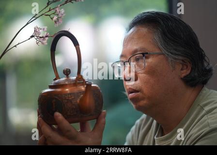 230815 -- NANCHANG, 15 août 2023 -- Huang Junjun regarde une théière de gravure sur cuivre dans son entreprise de Guixi City, province de Jiangxi dans l'est de la Chine, le 9 août 2023. Gravure sur cuivre, ou sculpture sur cuivre, un métier d'utilisation de couteaux pour sculpter des motifs sur des marchandises en cuivre, a une histoire d'environ 1 000 ans. En 2021, la gravure sur cuivre Guixi a été répertoriée comme l'un des patrimoines culturels immatériels au niveau national. L'artisanat a besoin de plus de 150 types différents de couteaux et une douzaine de compétences de sculpture pour créer une œuvre d'art complète, et la vaisselle en cuivre doit passer par plus de 100 000 fois de martelage avant d'être transformée en Banque D'Images