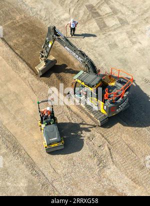 Pontyclun, pays de Galles - 7 septembre 2023 : vue par drone d'une excavatrice et d'une machine à rouleaux préparant le parking pour un développement de supermarché dans le sud du pays de Galles Banque D'Images