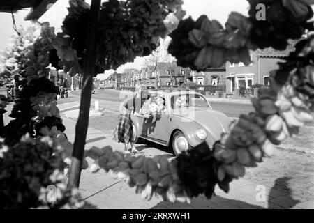 Eine junge Frau bietet Blumen zum Verkauf an der Straße an, im Vordergrund hängen Tulpengirlanden, lisse 1955. Une jeune femme propose des fleurs à vendre dans la rue, des guirlandes de tulipes sont suspendues au premier plan, lisse 1955. Banque D'Images
