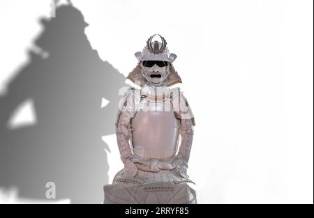 Découpe isolée d'une armure kachuu japonaise assise peinte en blanc avec un casque Kabuto et une armure de corps yoroi sur fond blanc avec un kagemusha shado Banque D'Images