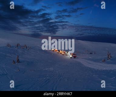 Tondeuses à neige (machines à ratraquer) en excursion nocturne avant l'aube jusqu'au sommet de la montagne en hiver avec des snowboarders freeriders. Station de ski alpin Dragob Banque D'Images