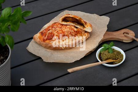 Pizza calzone découpée avec sauce tomate, pesto vert et fromage sur assiette en bois Banque D'Images