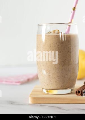 Smoothie cannelle banane poire en verre avec paille écologique sur la table avec fond blanc. Prise de vue verticale, gros plan. Boisson rafraîchissante naturelle aux fruits Banque D'Images