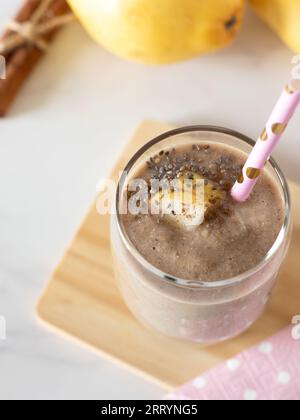 Smoothie à la poire et à la cannelle avec des graines de chia en verre avec de la paille écologique sur une table blanche. Prise de vue verticale, gros plan. Milk-shake de fruits sains pour la digestion. Banque D'Images