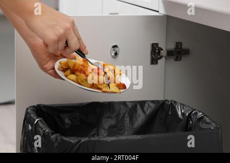 Femme jetant des pommes de terre cuites avec du ketchup dans la poubelle à l'intérieur, gros plan Banque D'Images